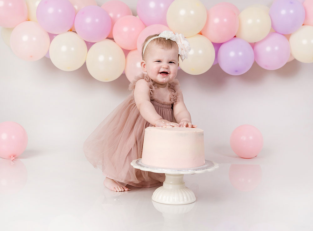 Baby at a 1st Birthday cake smash photoshoot with a pink cake and balloons