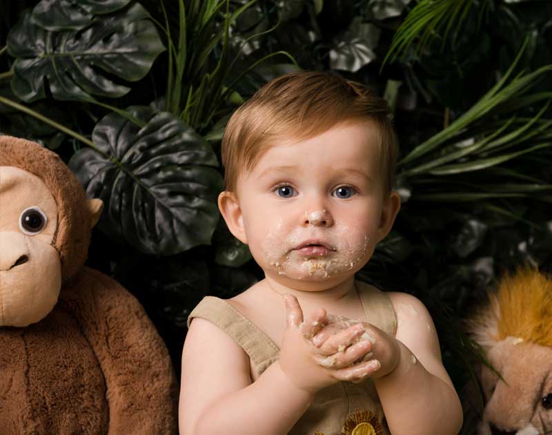 Little boy with cake on his face after a cake smash photo session in a jungle setting