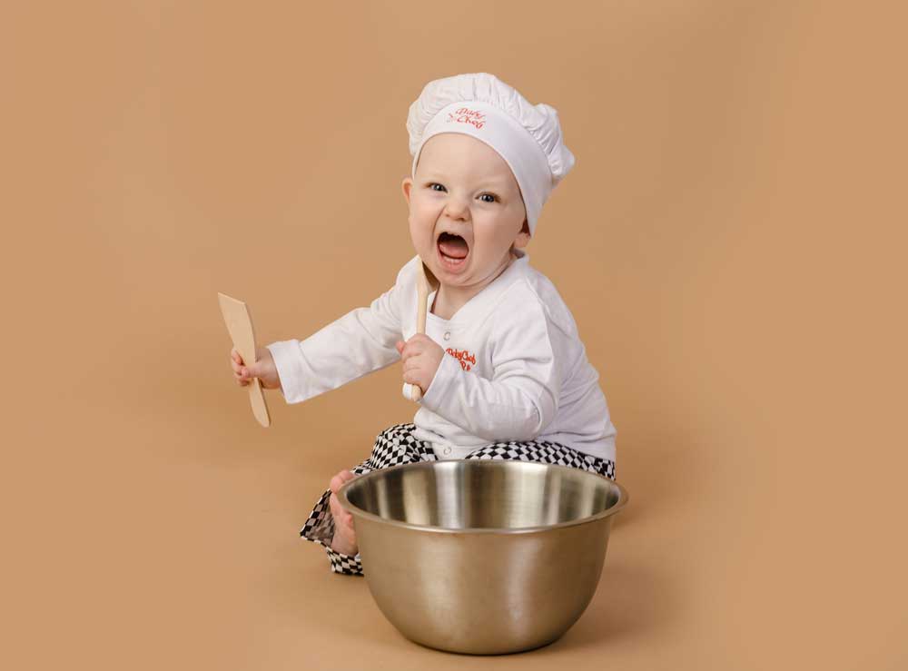 little boy dressed in a bakers outfit for a cake smash photoshoot