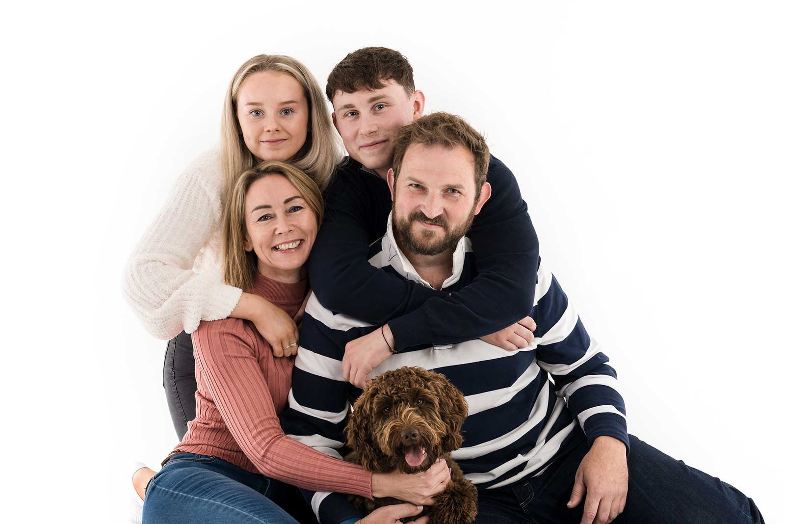 Family of 4 and a dog having a family portrait taken in a photography studio on a white background