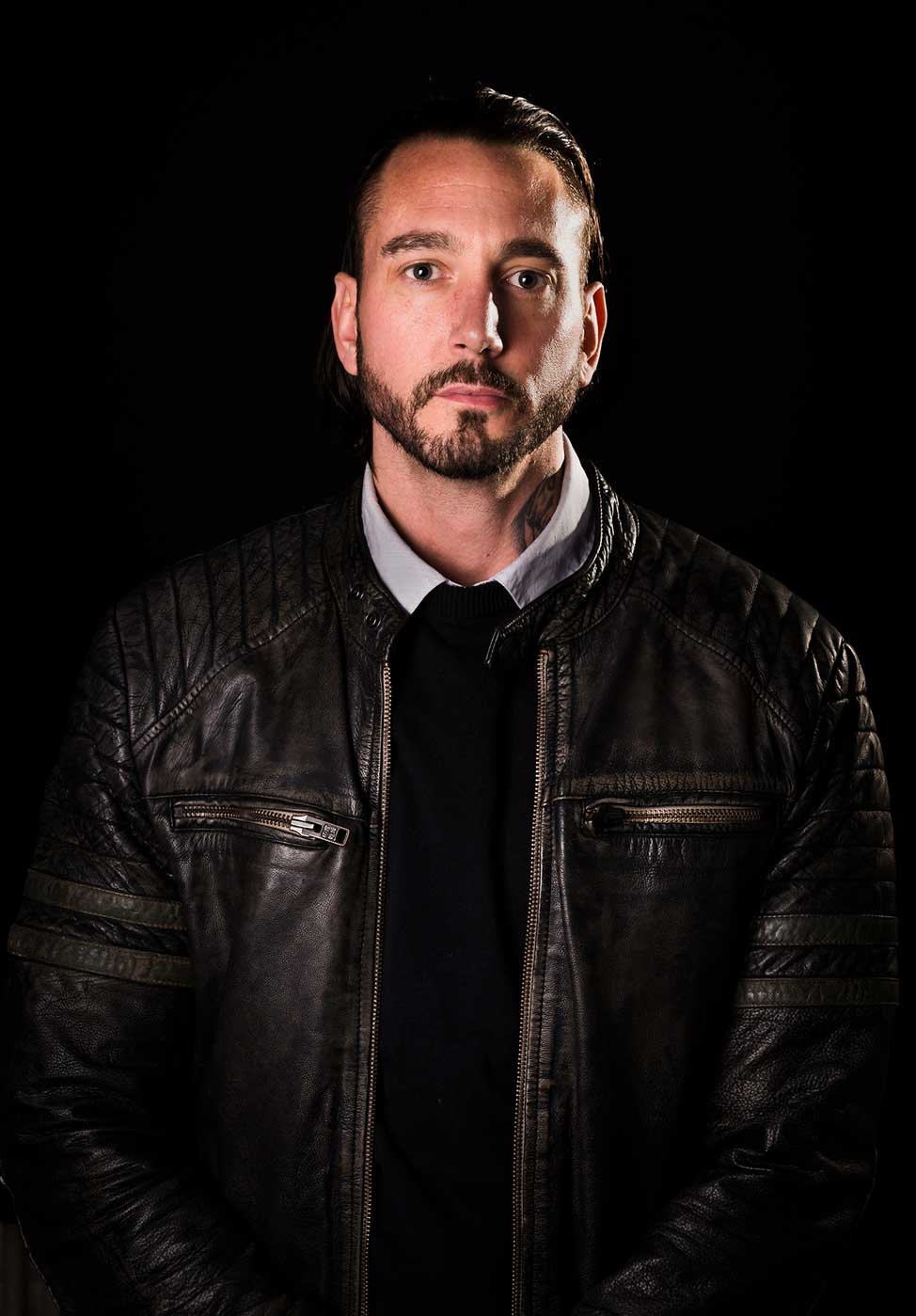 man looking at the camera for a corporate headshot with a dark background.