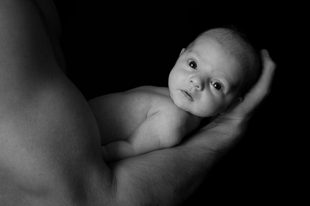Newborn baby in a mans hand for newborn photography session in black and white
