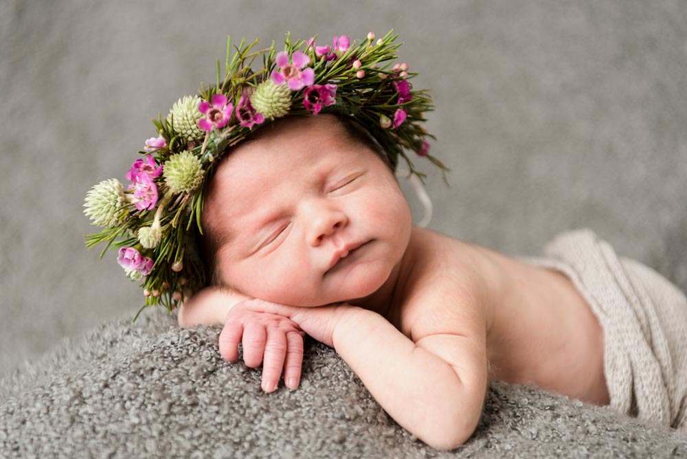 A small baby laying down asleep with flowers on her head for a newborn Photography session