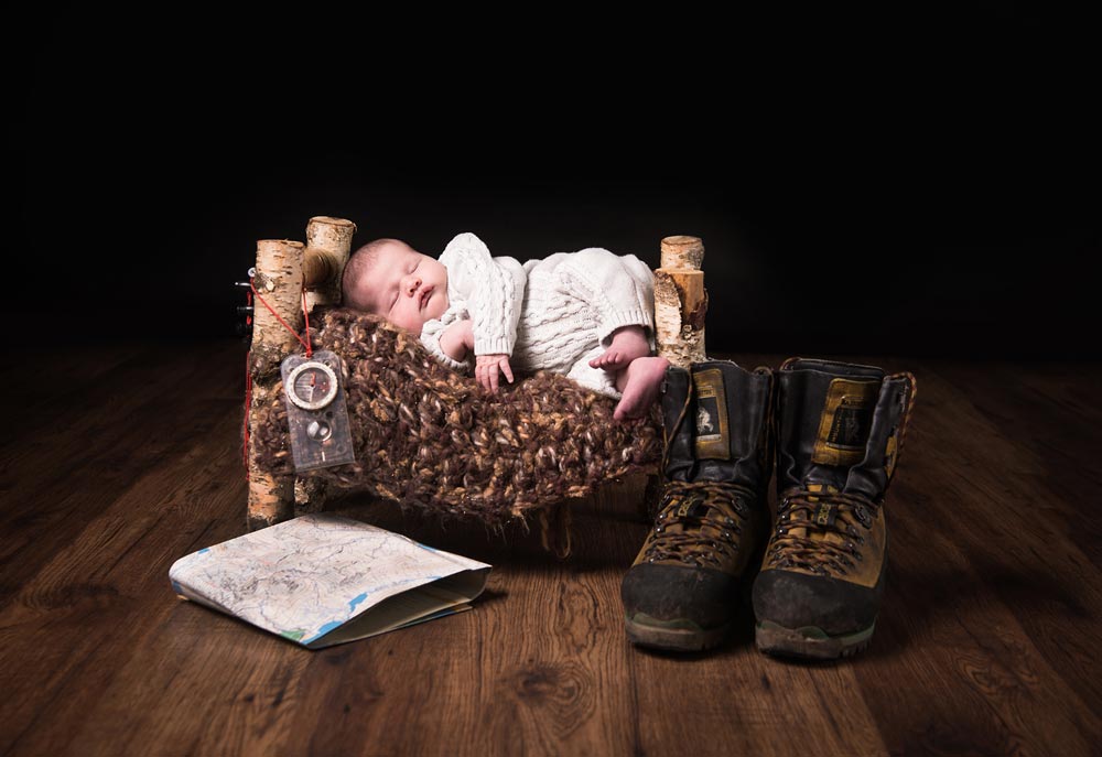 Newborn baby on a small bed with dads boots and map
