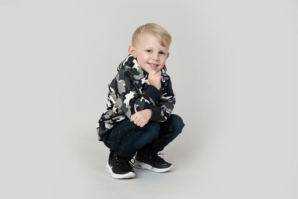 A boy crouching down smili8ng at a children's portrait photo shoot