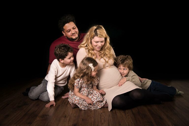 Family posing on the floor, mum is pregnant and showing her bump for a bump to baby photoshoot Experience